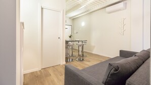 En moderne stue med en grå sofa, trægulv og et hvidt loft med ovenlys.