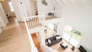 A spacious loft apartment with a high ceiling, wooden floors, a black sofa, a dining area, and a balcony with a view. - Ferienhaus DeichGalerie89 (Krummhoern)
