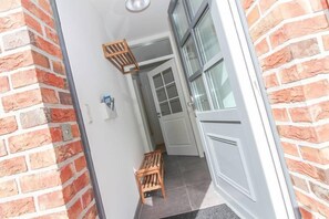 A hallway with a brick wall, a white door, and a small wooden bench. - Ferienhaus DeichGalerie89 (Krummhoern)