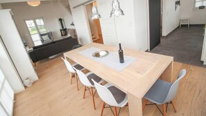A dining area with a wooden table, white chairs, and pendant lighting. - Ferienhaus DeichGalerie89 (Krummhoern)