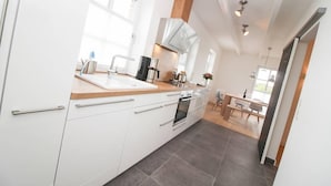 A modern kitchen with white cabinets, a wooden countertop, and a built-in oven. - Ferienhaus DeichGalerie89 (Krummhoern)