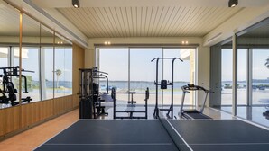 Una palestra con attrezzature, ampie finestre e vista sul mare.