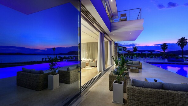 Un'area relax esterna moderna con piscina, posti a sedere e vista sul mare al crepuscolo.