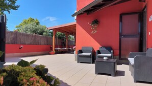 An outdoor patio with wicker furniture, a red building, and a wooden fence. - B&B Felicioni (Fiumicino)