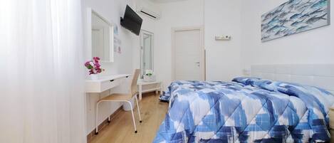 A bedroom with a bed, a desk, a chair, and a TV mounted on the wall.