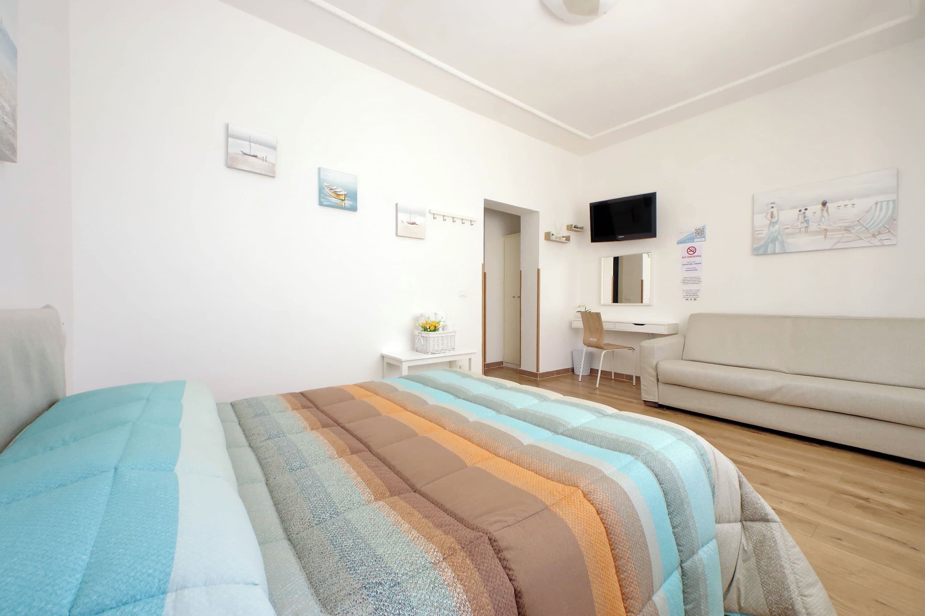 Um quarto com cama, escrivaninha, sofá e obras de arte nas paredes.