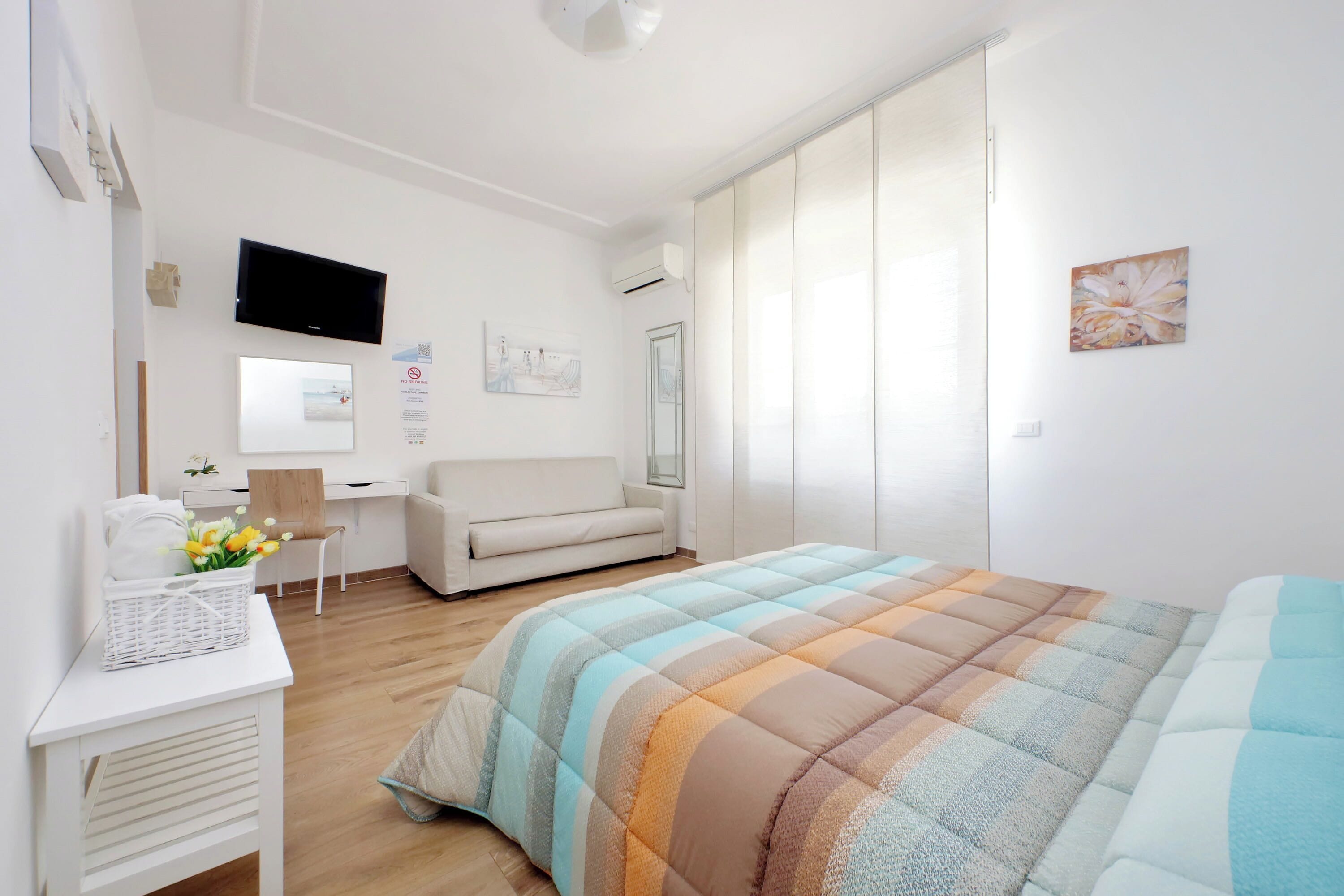 A modern bedroom with a bed, a desk, a chair, and a TV.
