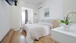 A modern bedroom with a bed, a bedside table, a TV mounted on the wall, and a potted plant. - B&B Felicioni (Fiumicino)