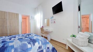 A hotel room with a bed, a desk, a TV, a mirror, and a basket of towels.