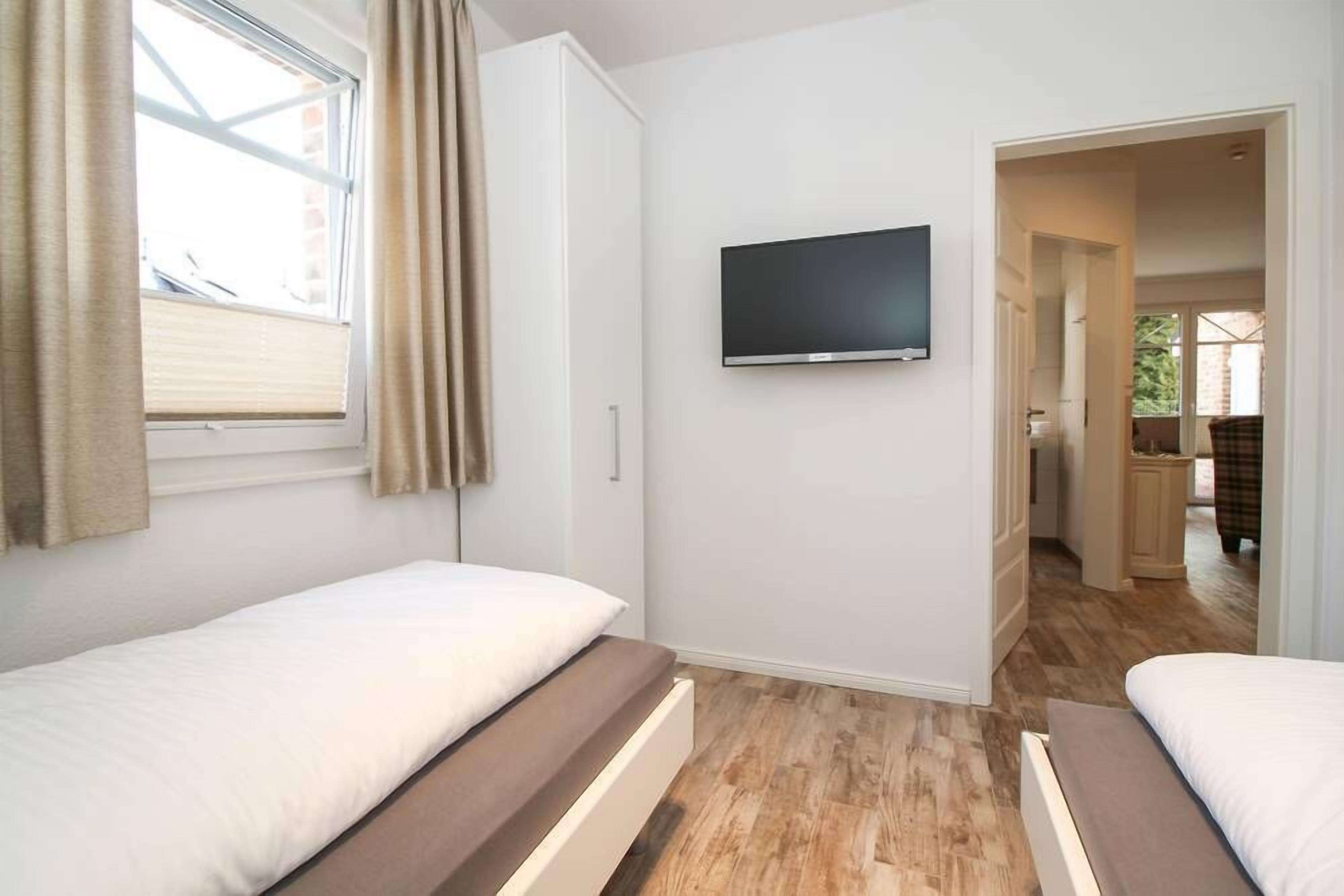A bedroom with two beds, a TV, and a window with curtains.
