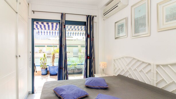 A bedroom with a bed, two purple pillows, a white headboard, and a view of an outdoor balcony with potted plants. - Playa Azul , Luxury Penthouse With Spectacular Roof Terrace (Mogan)