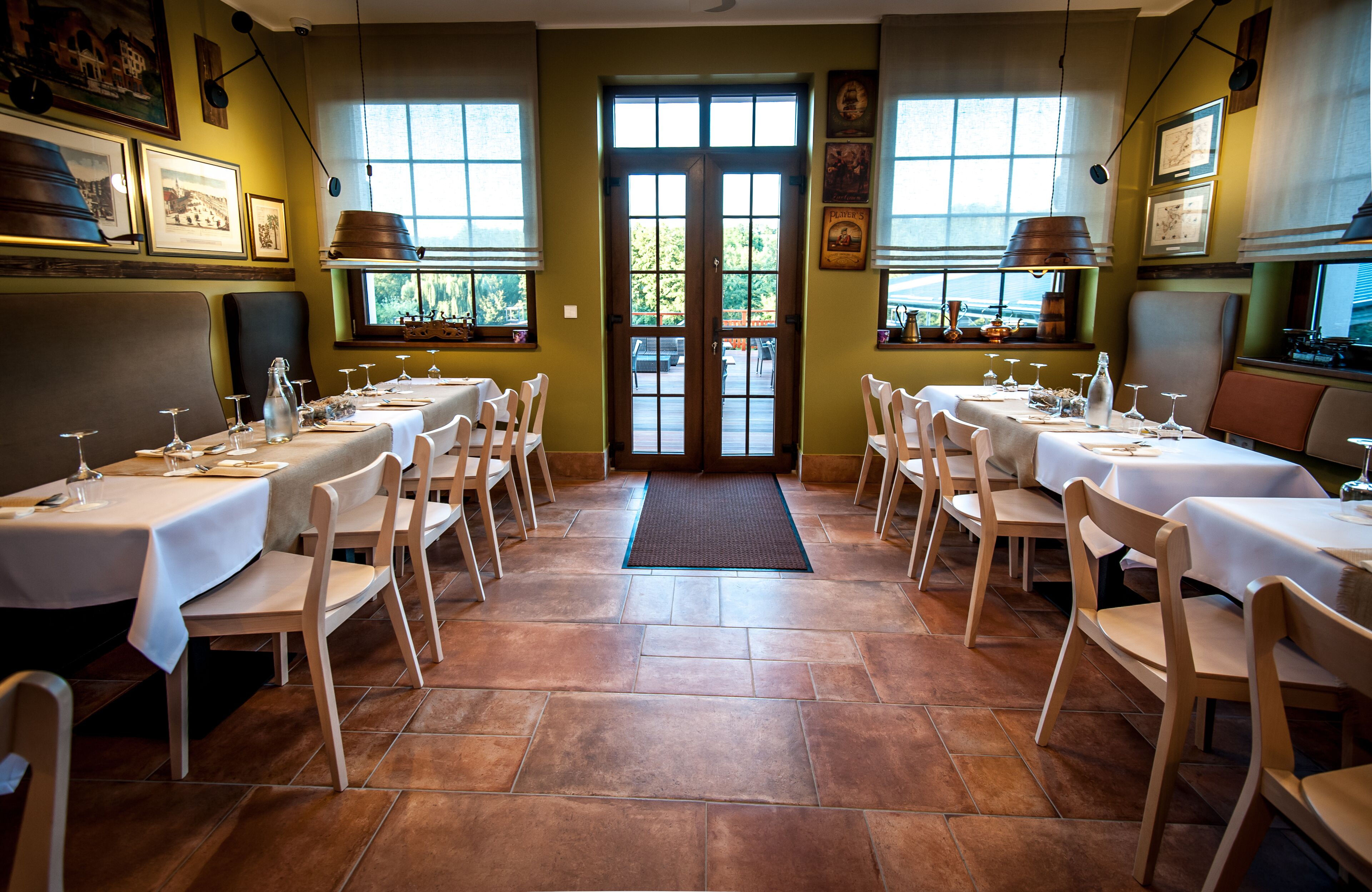 A restaurant with multiple tables and chairs, a tiled floor, and large windows.