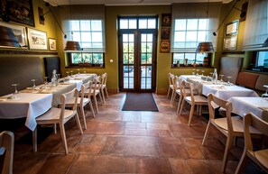 A restaurant with multiple tables and chairs, a tiled floor, and large windows.