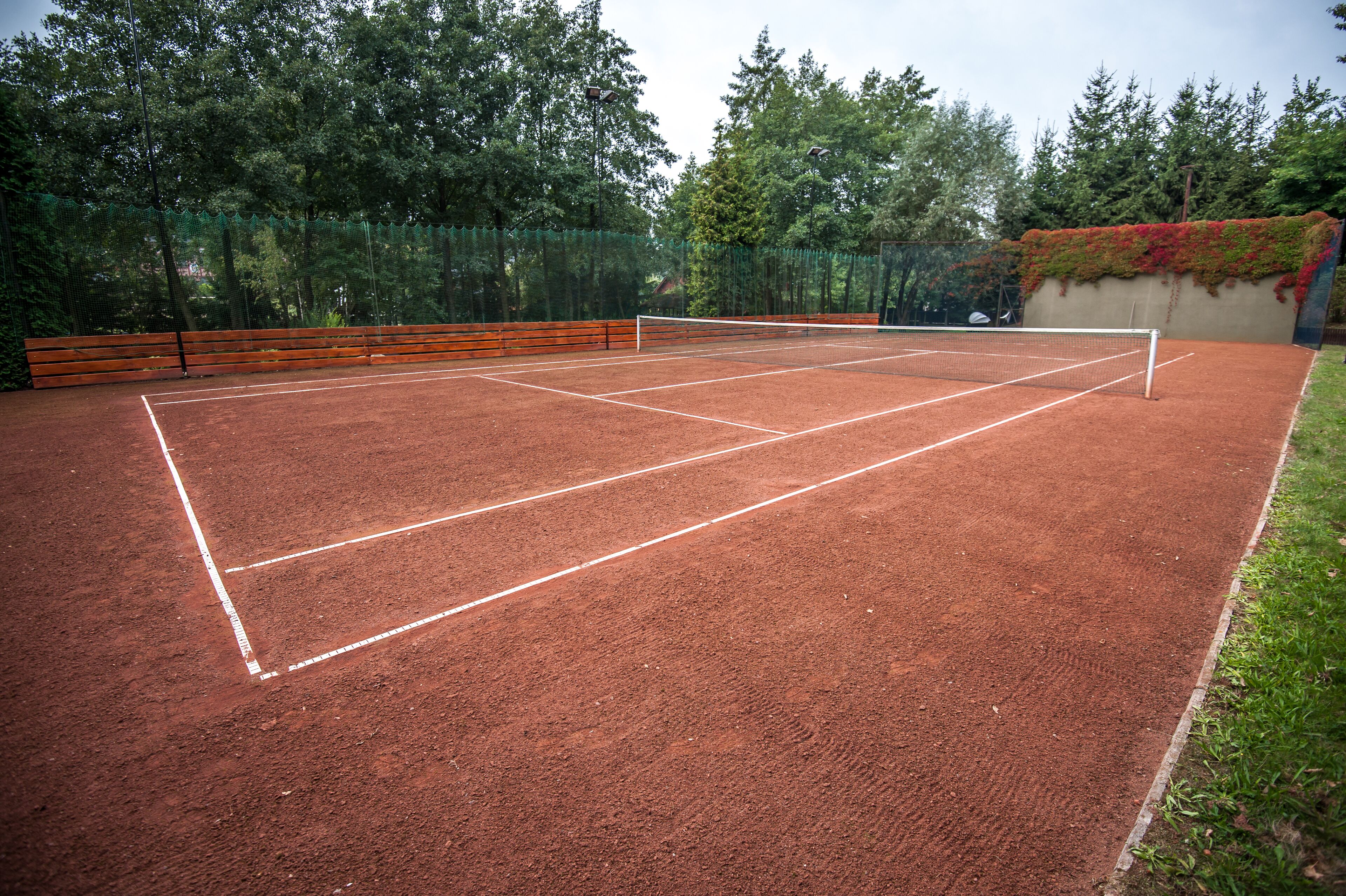 A tennis court with a net, surrounded by a fence and trees.