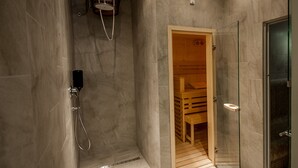 Un baño moderno con ducha de vidrio, puerta de sauna de madera y piso de baldosas.