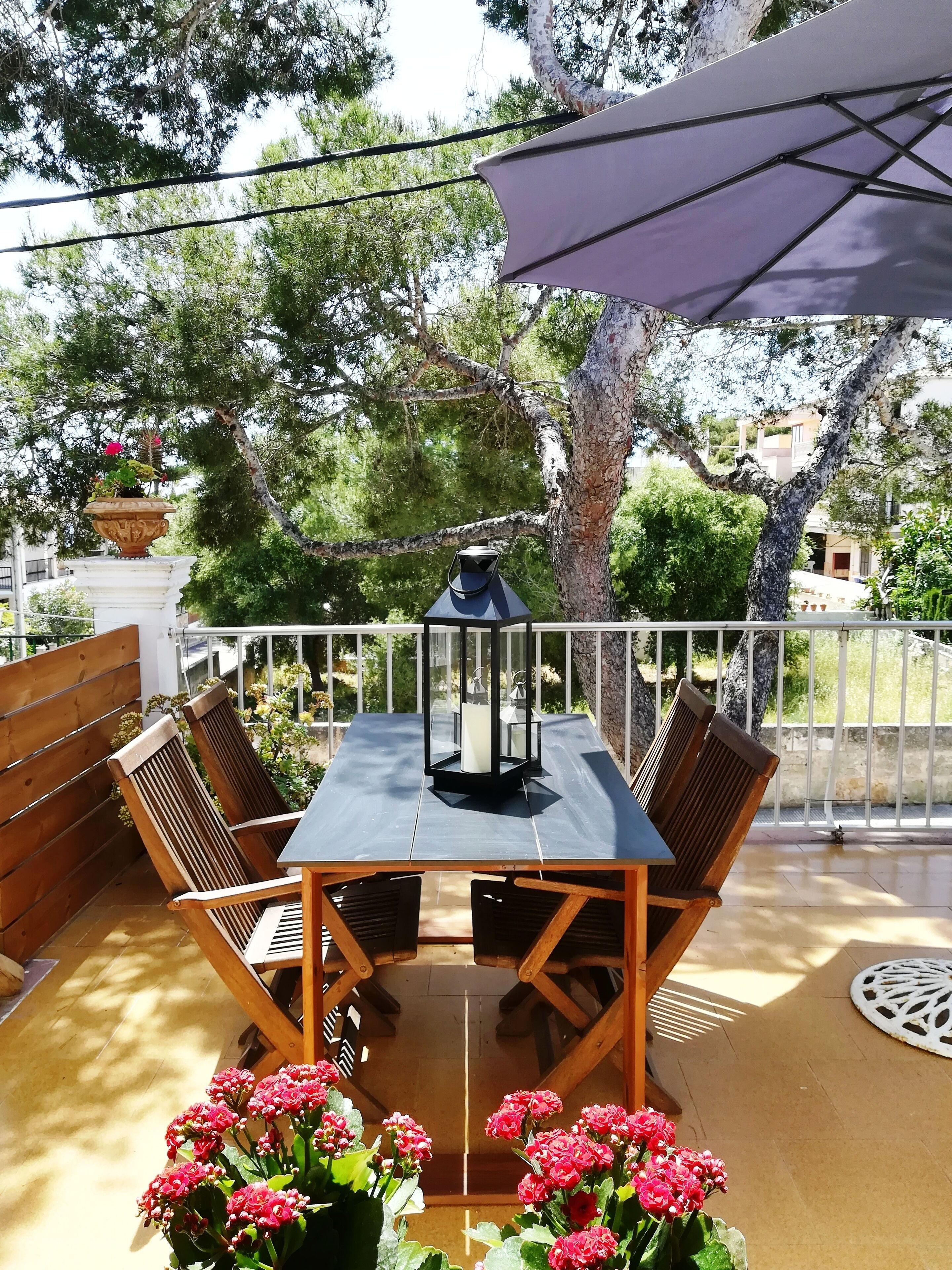 A wooden table with chairs, a lantern, and potted flowers on an outdoor patio.