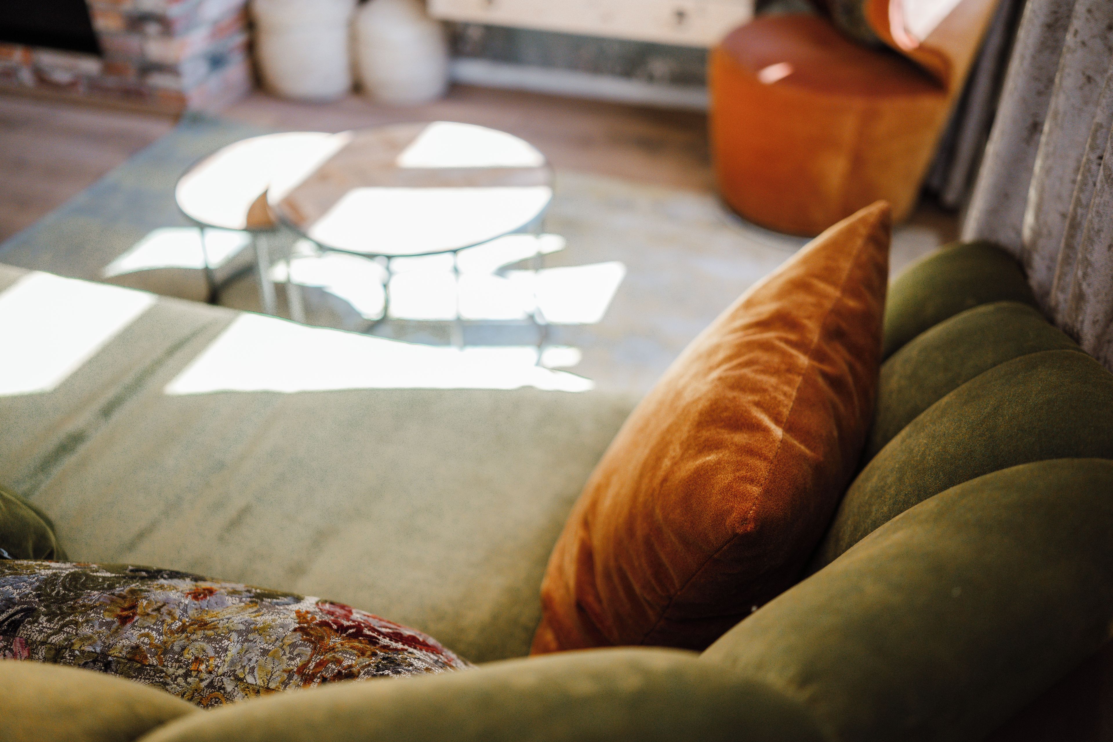 Un canapé vert avec un coussin à motifs et un seul coussin orange.