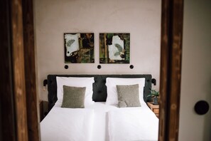 A double bed with two pillows, a dark headboard, and two abstract wall art pieces above it.