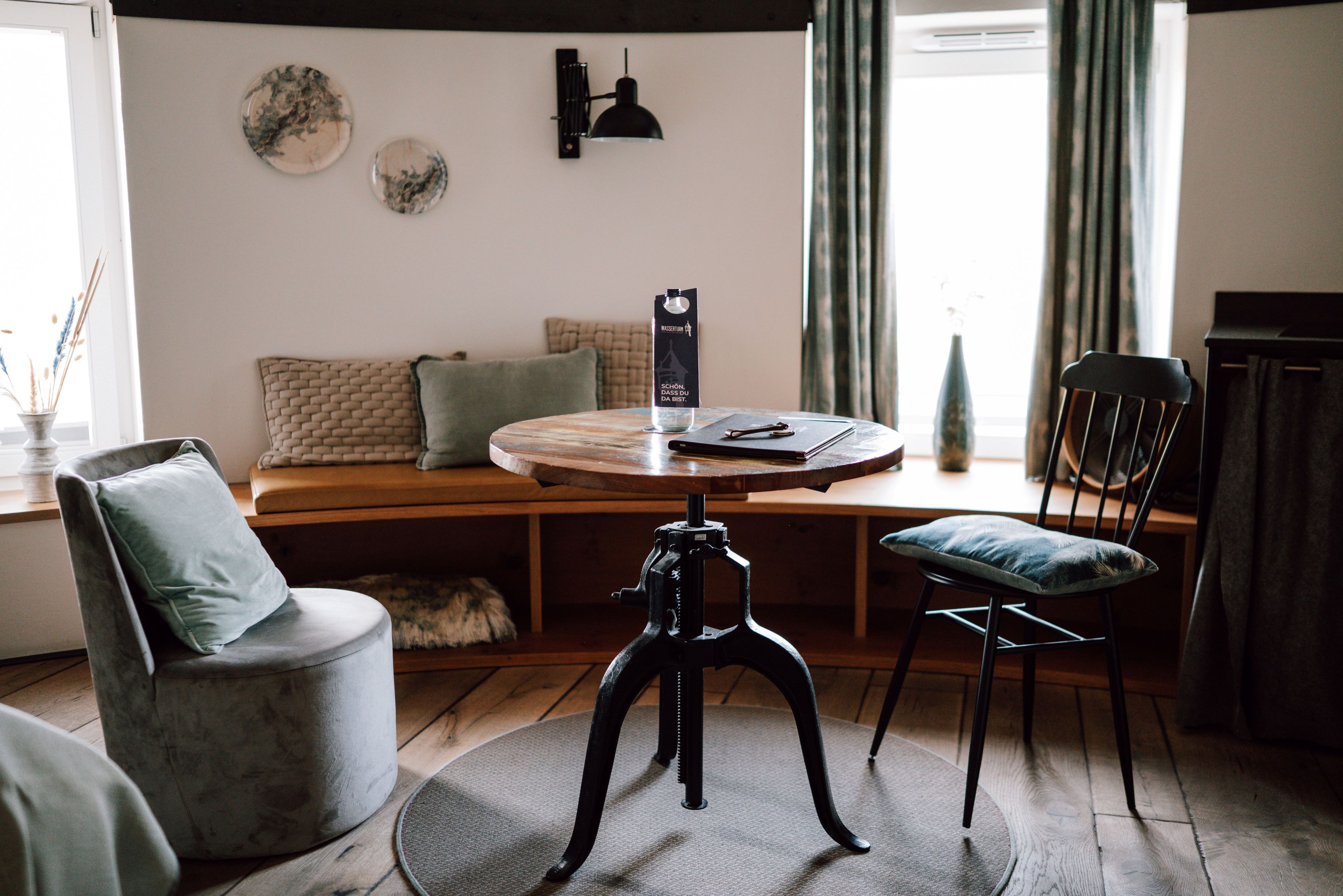 A cozy living room with a round wooden table, two chairs, a sofa, and a small dog.