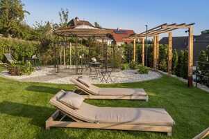 Un jardín con dos sillones de descanso, una pérgola y un pabellón.