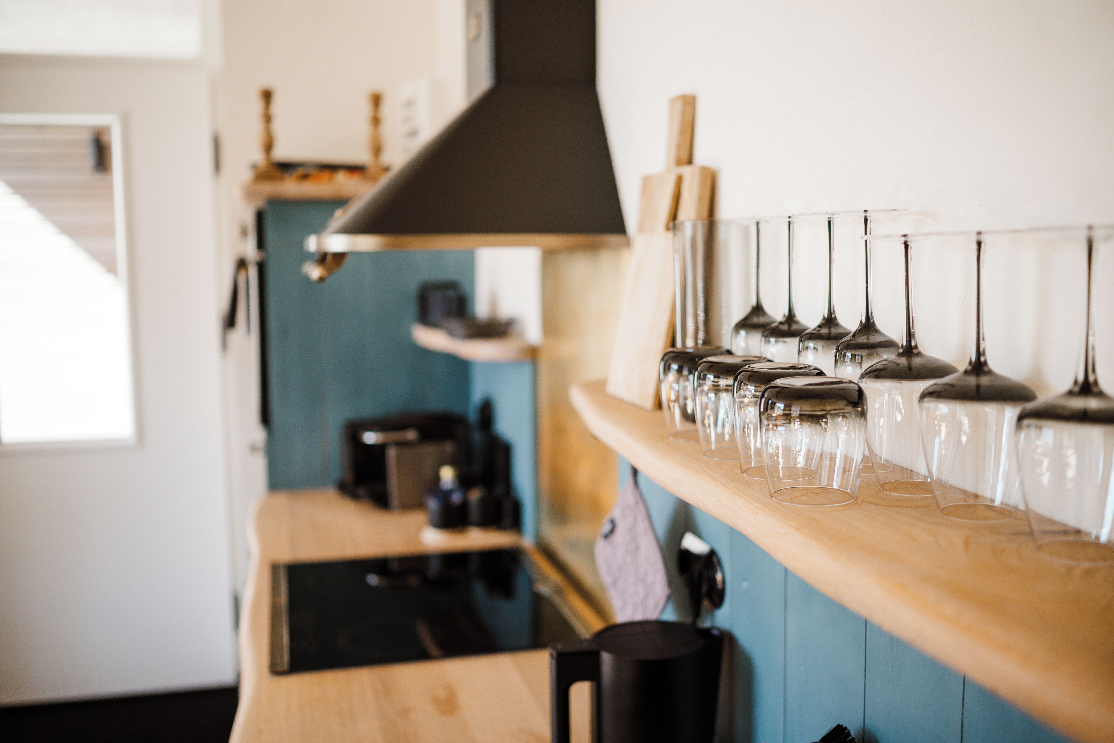 Une cuisine avec un plan de travail en bois, une machine à café et une rangée de verres à vin disposés sur une étagère.