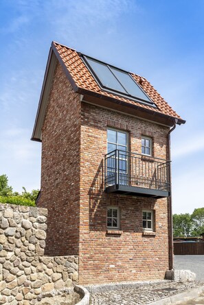 A two-story brick building with a balcony and a stone wall. - Apart Hotel Wasserturm (Bad Segeberg)