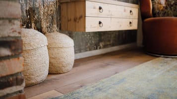 A wooden dresser with drawers, two woven poufs, and a red chair in a room with a wooden floor and a textured wall.