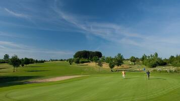 Un campo de golf con cielo despejado, árboles y un césped bien cuidado.