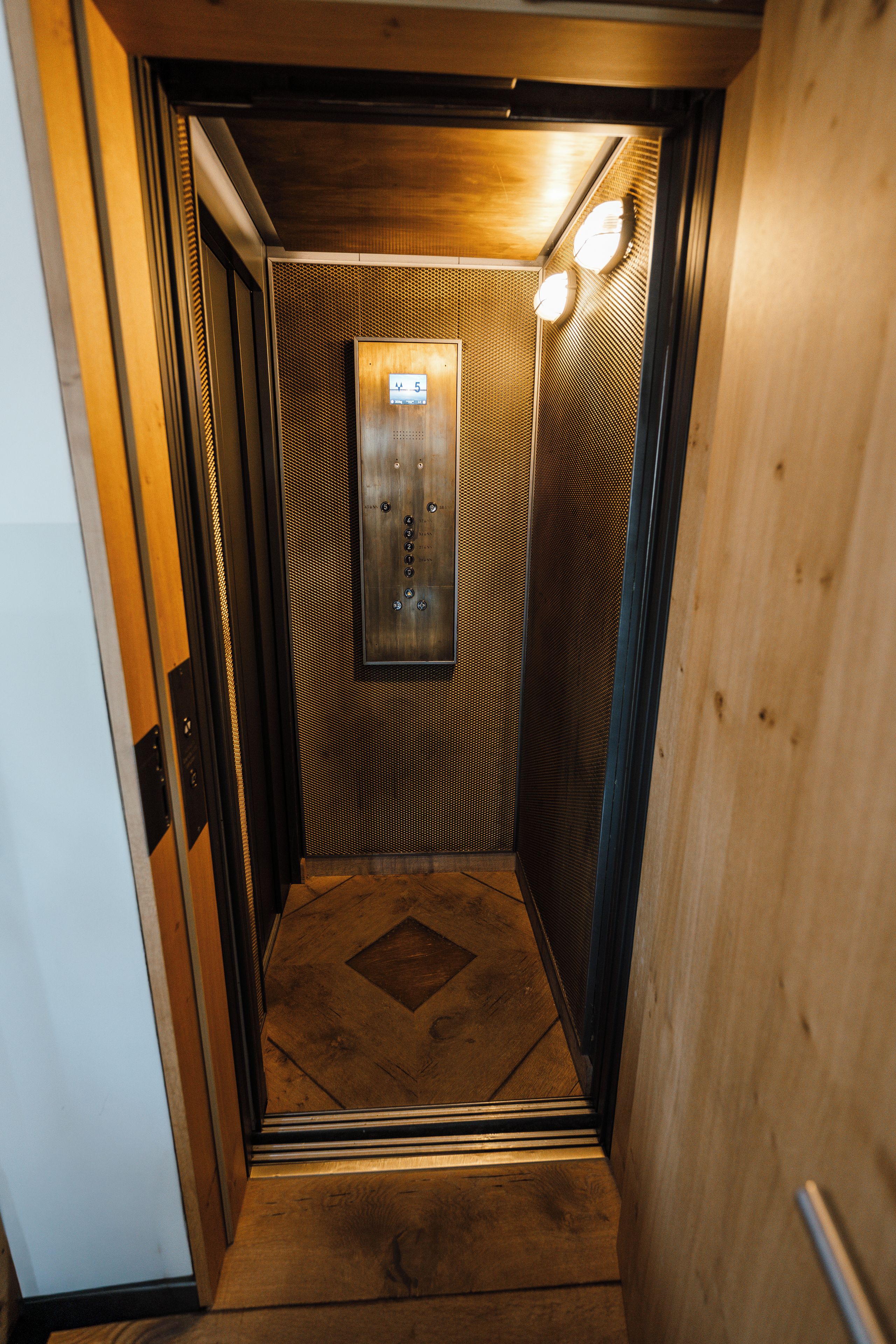 Interior de ascensor con detalles de madera, pantalla digital y pared con textura.