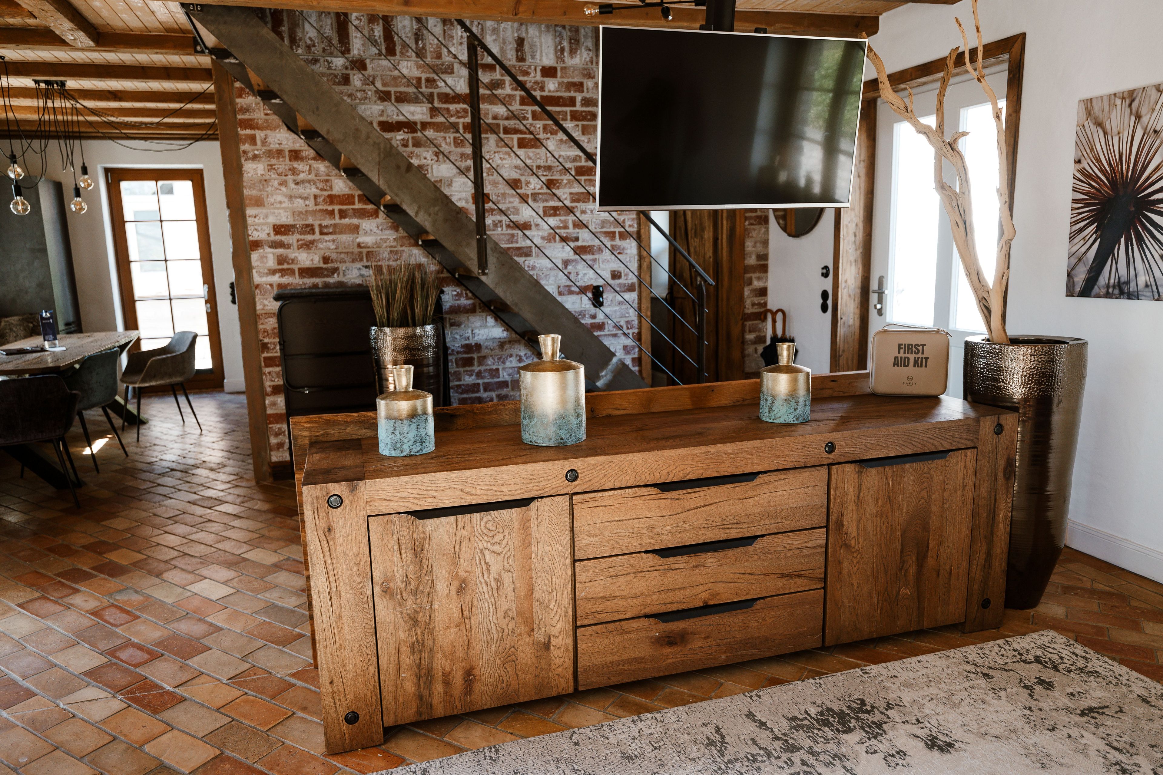 A rustic wooden bar with a television mounted above it, a brick wall, and a staircase in the background.