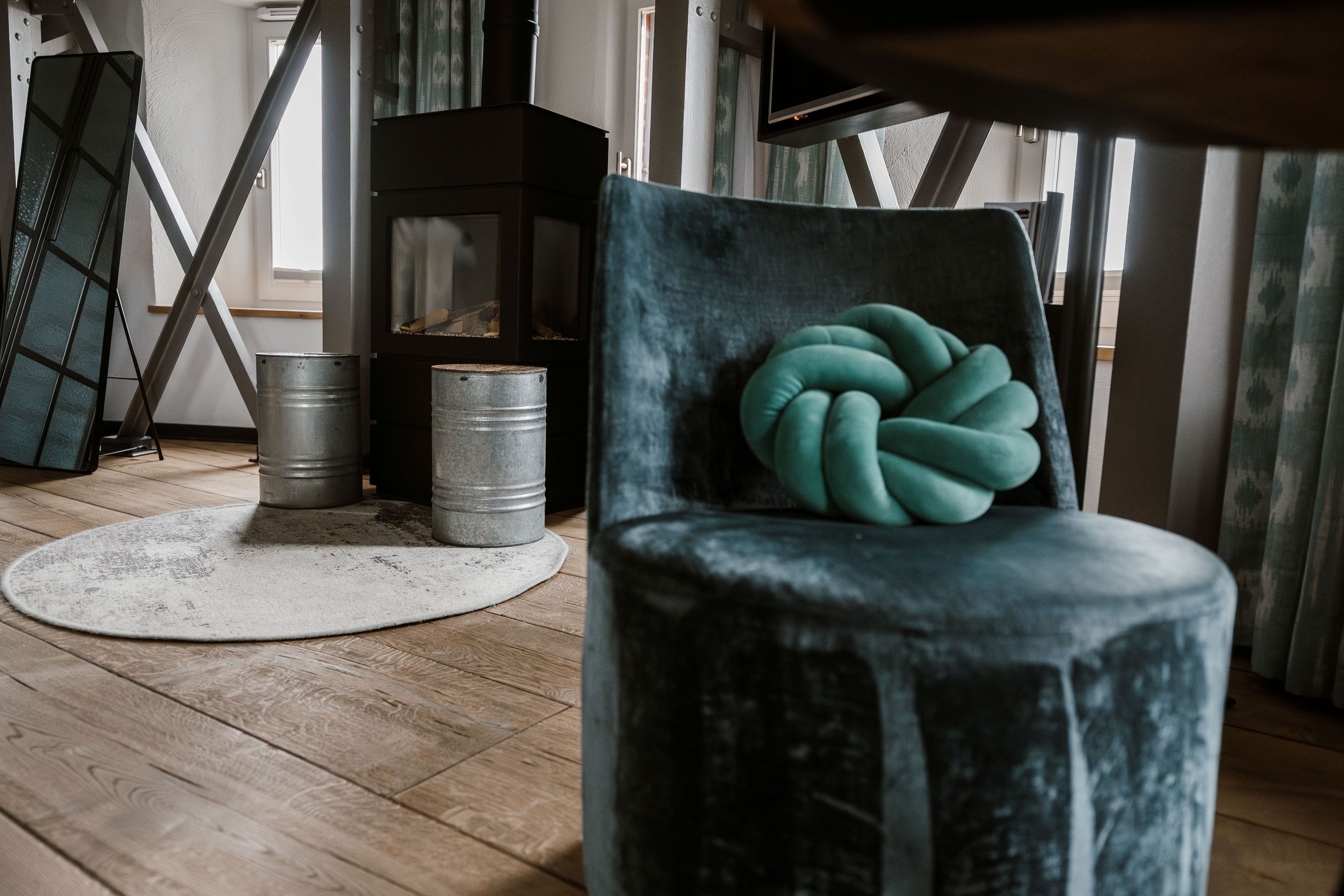 A room with a wooden floor, a round rug, a metal barrel, and a chair with a unique cushion.