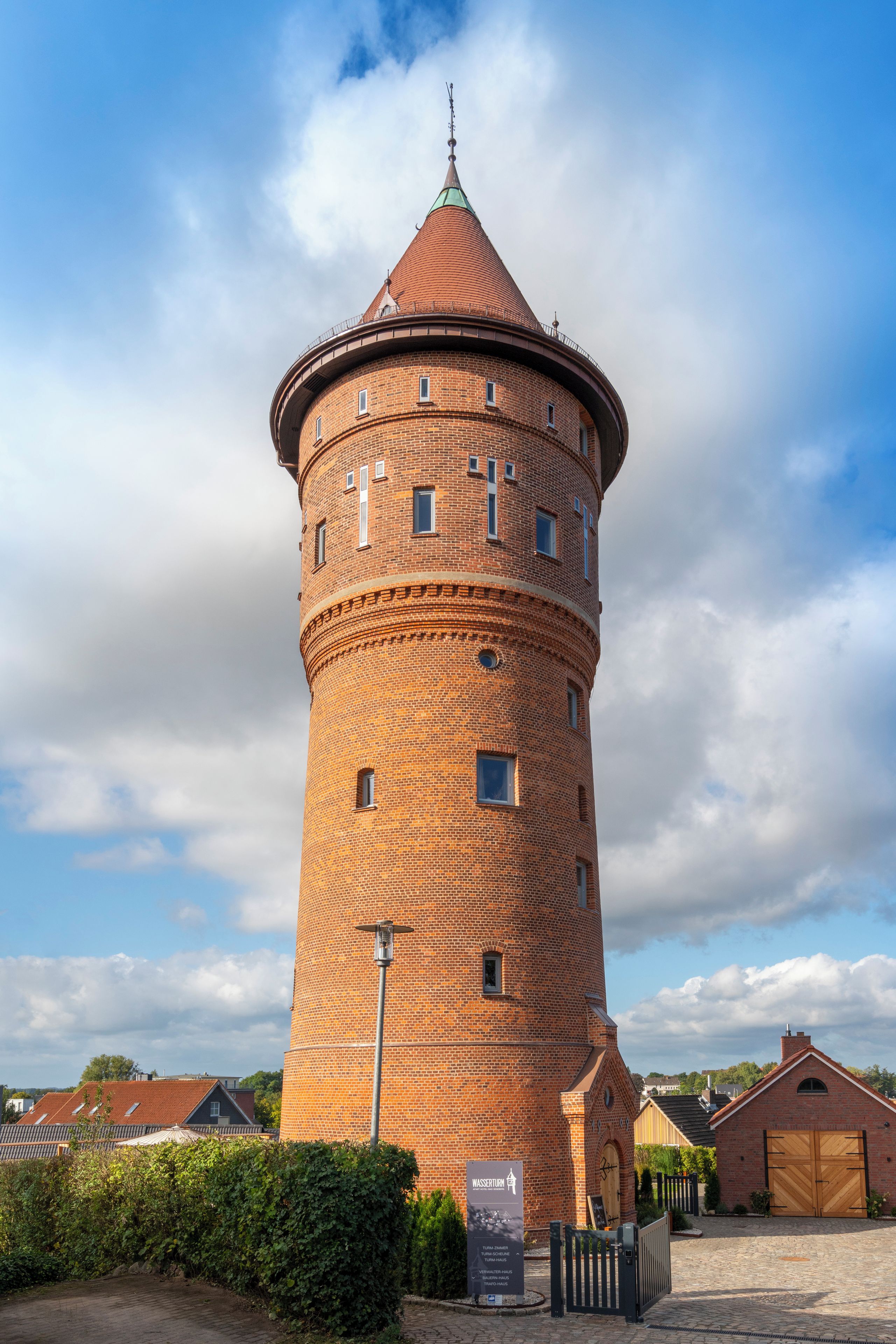 A brick tower with a conical roof, surrounded by a paved area with a gate and a signboard.