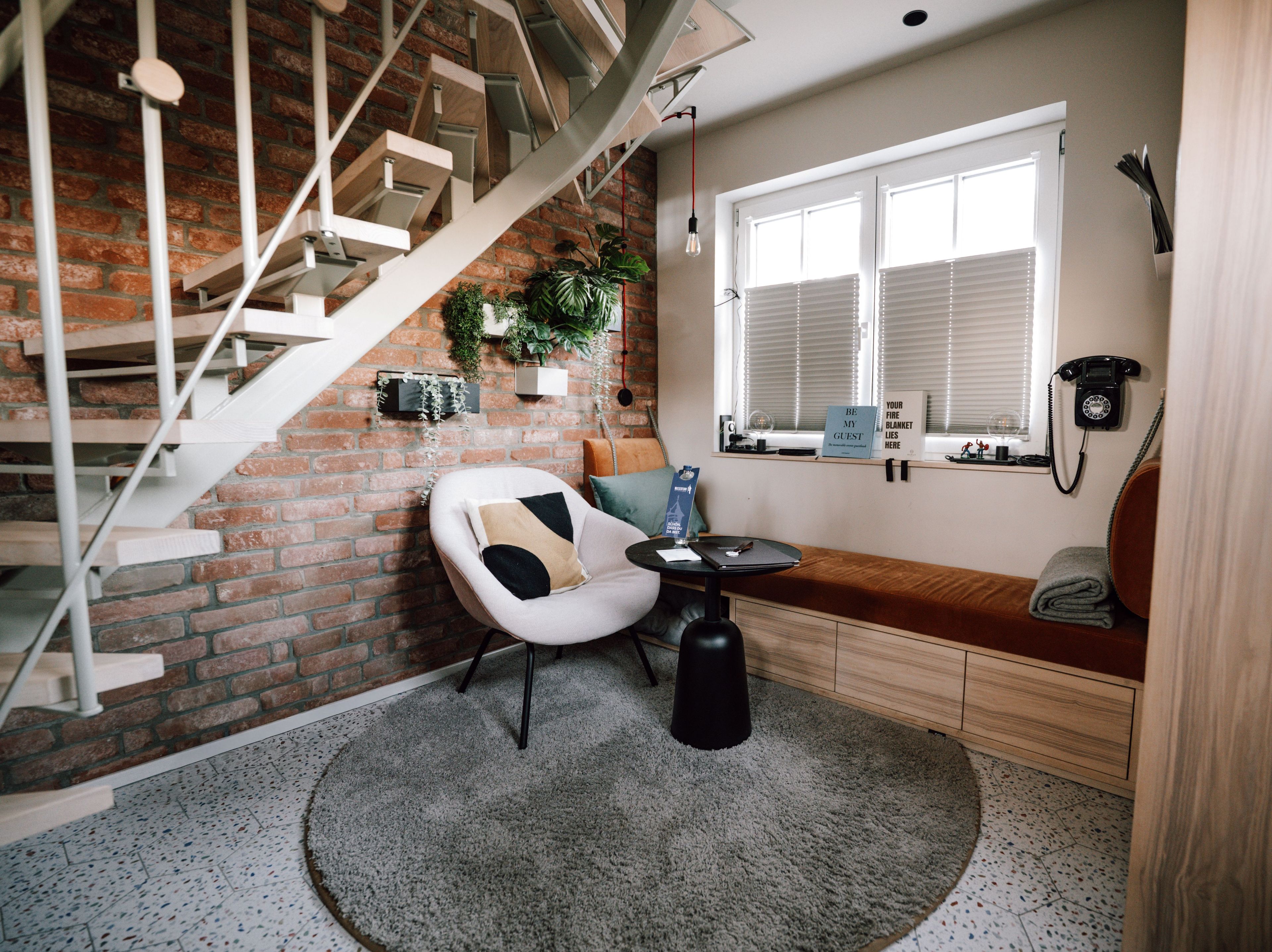 A modern interior with a spiral staircase, a seating area with a cushioned chair, a small table, and a window with blinds.