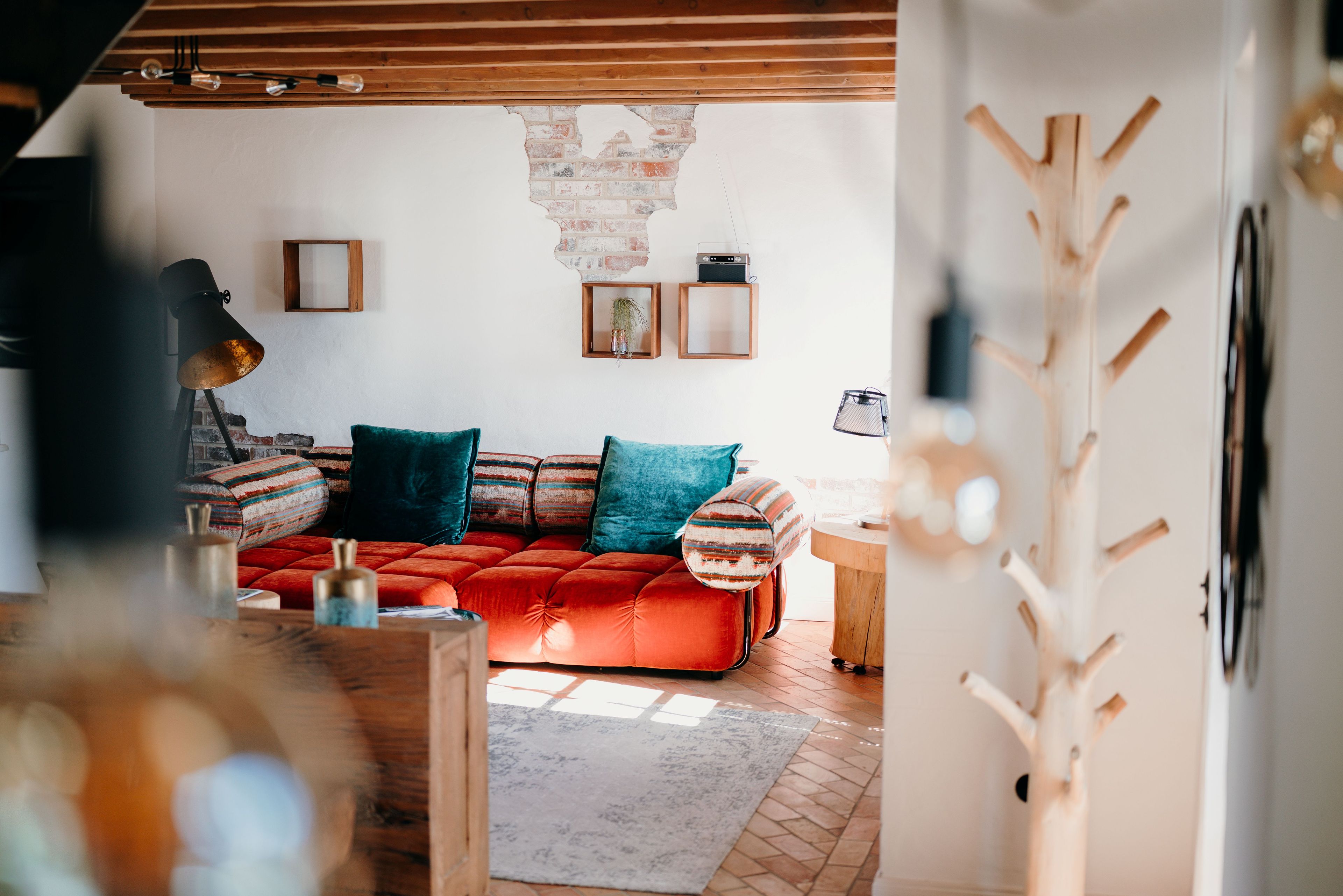 Una sala de estar acogedora con un sofá rojo, cojines estampados y techo de madera.