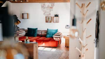 Una sala de estar acogedora con un sofá rojo, cojines estampados y techo de madera.