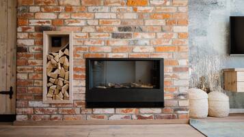 A fireplace with a brick wall, a wooden shelf with logs, and a flat-screen TV mounted on the wall.
