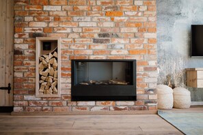 A fireplace with a brick wall, a wooden shelf with logs, and a flat-screen TV mounted on the wall.