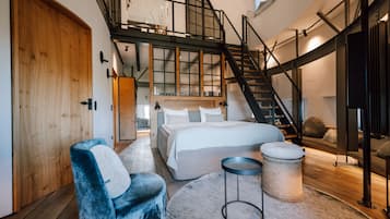 Ein Schlafzimmer mit einem großen Bett, einem Sessel, einem runden Tisch und einer Treppe, die zu einer oberen Ebene führt.