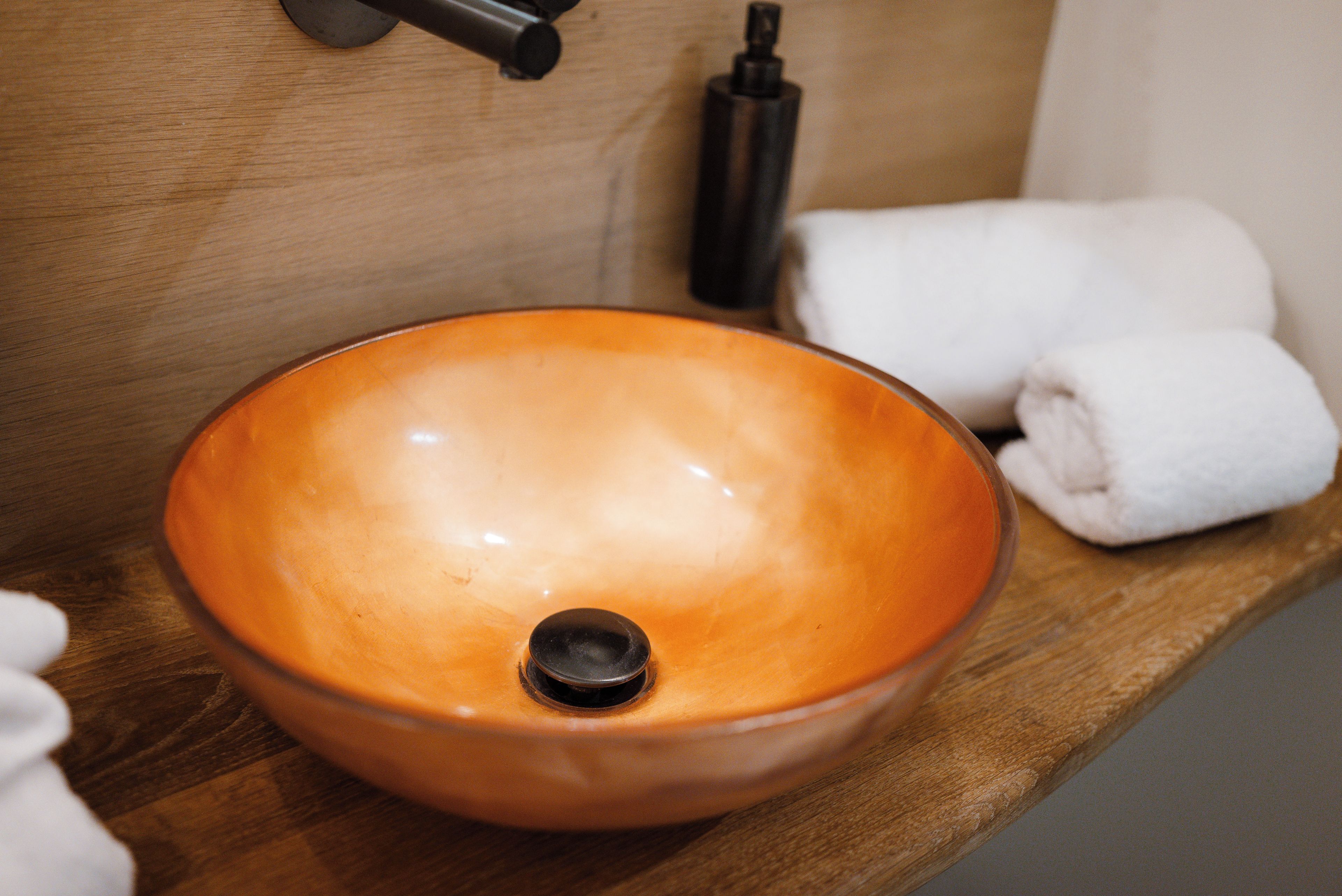A bathroom with a wooden shelf, a round sink, and towels.