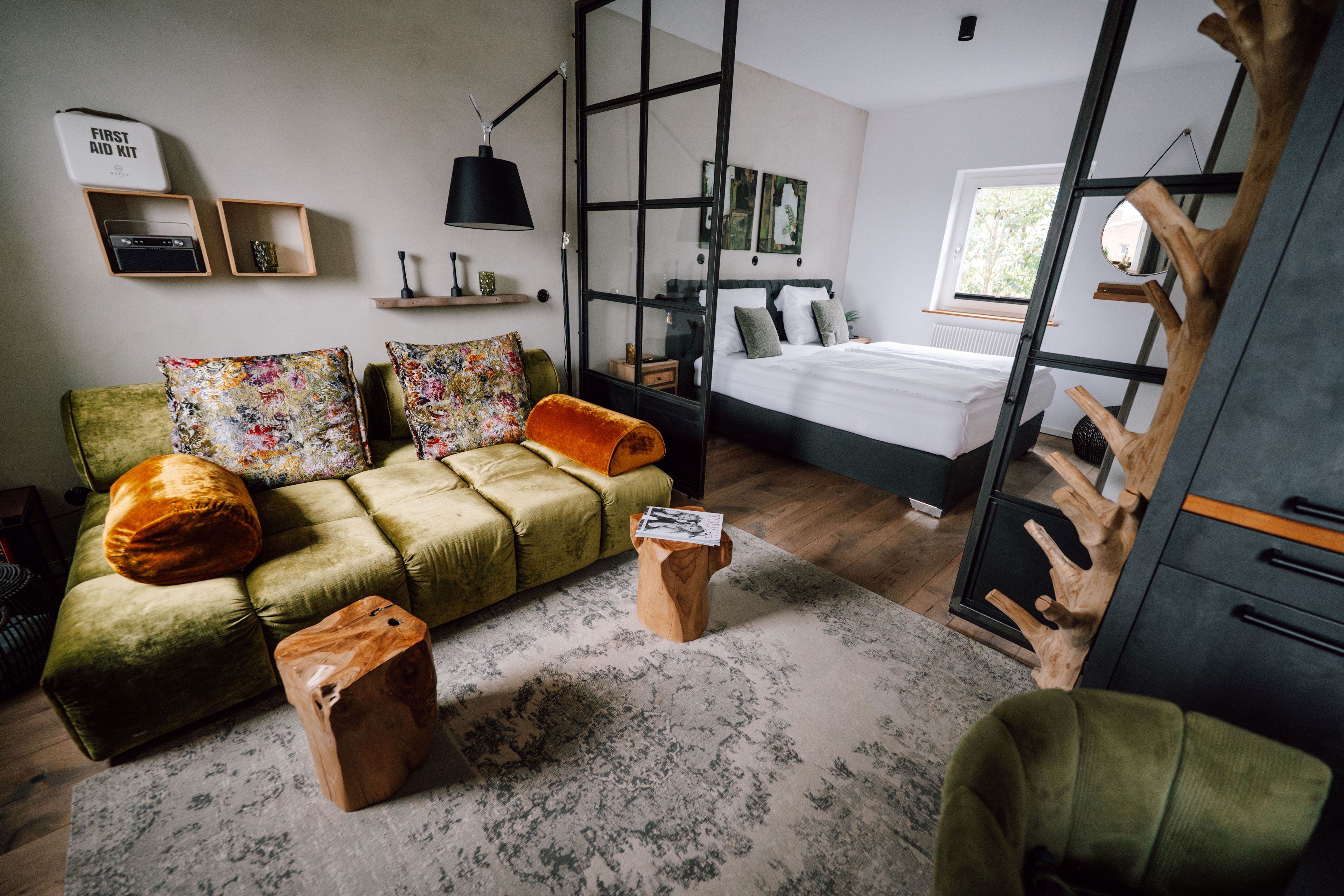 A modern bedroom with a green sofa, a wooden coffee table, and a bed with green pillows.
