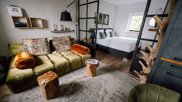 A modern bedroom with a green sofa, a wooden coffee table, and a bed with green pillows.