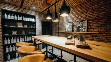 Zona de bar con pared de ladrillo, mesa de madera, taburetes de cuero y estanterías llenas de botellas de ginebra.