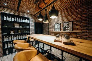 Zona de bar con pared de ladrillo, mesa de madera, taburetes de cuero y estanterías llenas de botellas de ginebra.