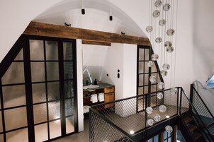 Interior moderno com um quarto estilo loft, teto de madeira, área de cozinha com pia e bancada, e escada com corrimão de metal.