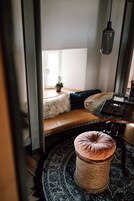Una habitación acogedora con una cama, un otoman tejido redondo, una mesita con una caja y una lámpara colgante.