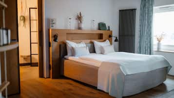 A bedroom with a wooden headboard, a large bed with white bedding, a bedside table, a lamp, and a window with curtains.
