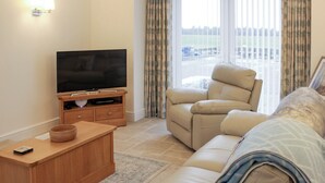 A living room with a flat-screen TV on a wooden stand, a beige sofa, and a recliner.