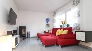 Uma sala de estar moderna com um sofá vermelho, uma televisão de tela plana, lareira e uma janela com detalhes decorativos.
