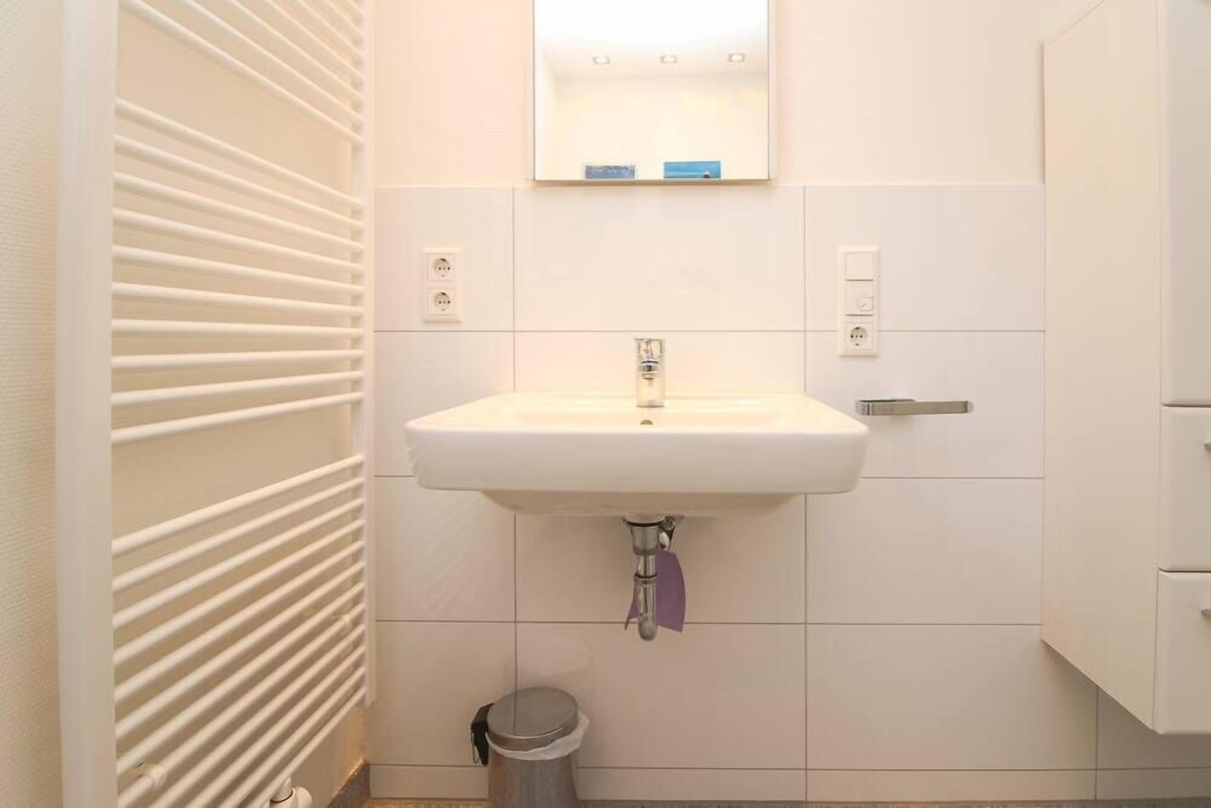A bathroom with a white sink, a mirror above it, and a trash bin to the left.