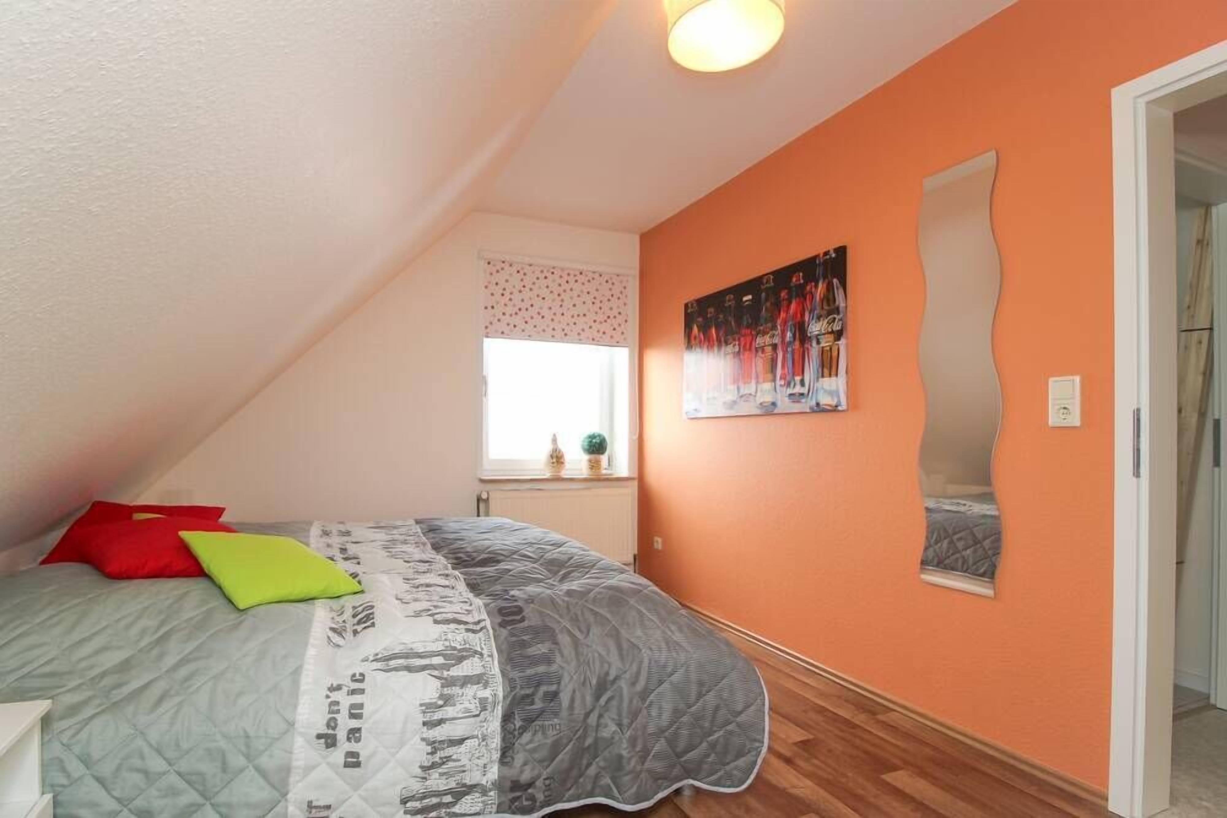 A bedroom with a sloped ceiling, a bed with a quilt, pillows, a window with a view, and a wall-mounted mirror.